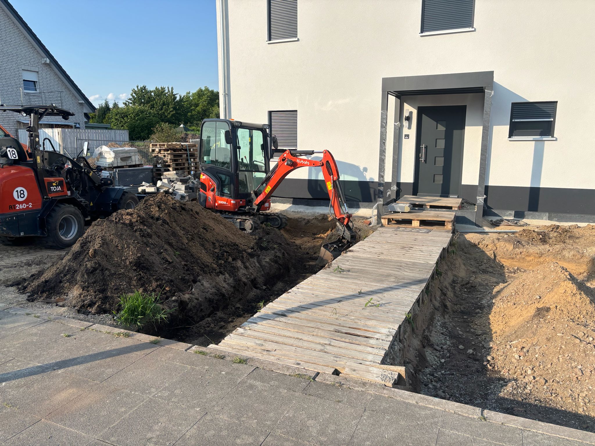 Kubota-Minibagger und Radlader beim Aushub eines Grabens am Neubau – Erdbauarbeiten