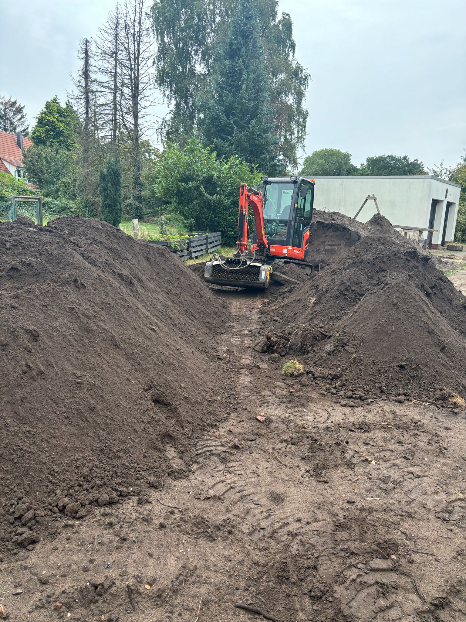 Kubota-Minibagger zwischen zwei Erdwällen beim Aushub – Erdarbeiten und Geländemodellierung
