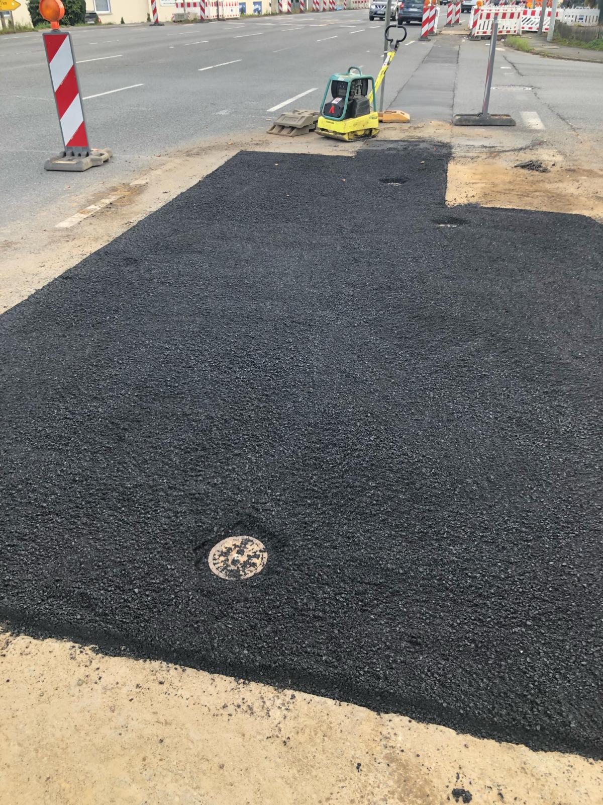 Frisch asphaltierte Verkehrsfläche mit Rüttelplatte und Baustellenabsicherung