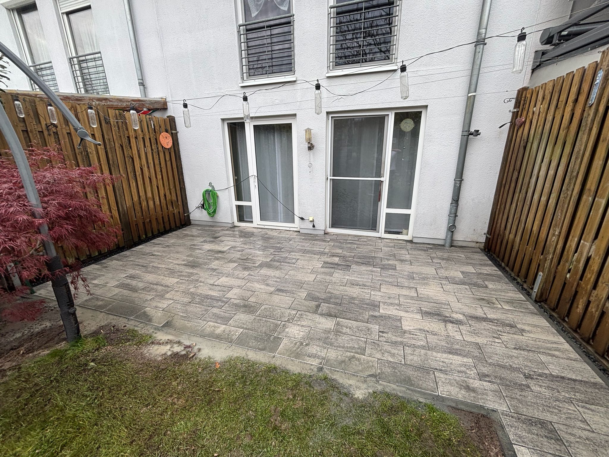 Kleine Hofterrasse mit grauen Pflasterplatten zwischen Holzzäunen