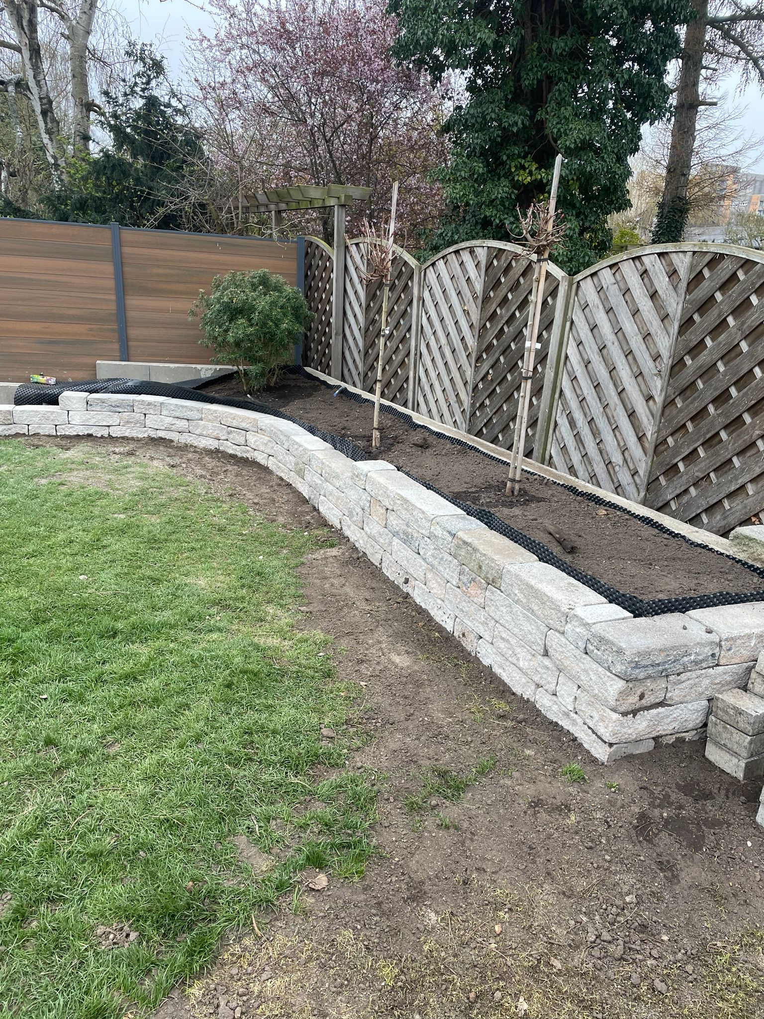 Geschwungene Natursteinmauer mit Pflanzbeet im Garten